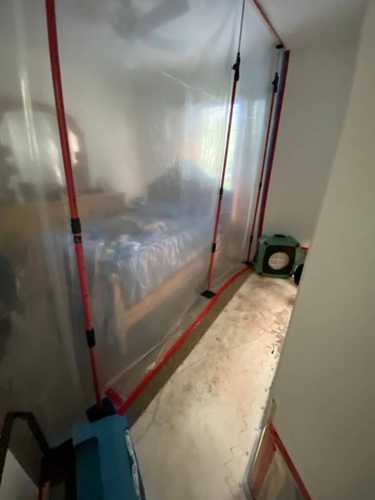 Sealed plastic containment with negative air pressure protecting a bedroom during mold remediation
